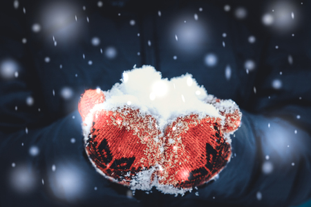 girl in red mitten holding a handful of snow close-up during snowfall. Beautiful snowy winter conceptual image filterの写真素材