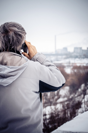 An elderly man talking on the phone and looking at plant close-up. Old man outdoors European Caucasian winter on a cloudy dayの写真素材