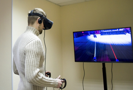 Man in helmet virtual reality plays game. Man uses VR-headset display with headphones for virtual reality game in office. High-tech devices. Augmented reality device creating virtual spaceの写真素材