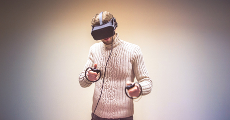 Man in helmet virtual reality plays game. Man uses VR-headset display with headphones for virtual reality game in office. High-tech devices. Augmented reality device creating virtual spaceの写真素材