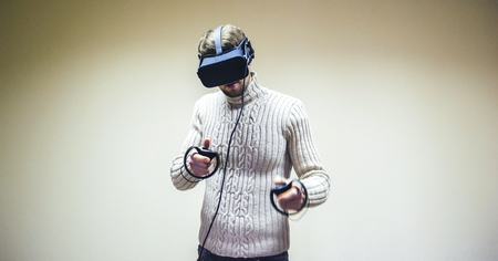 Man in helmet virtual reality plays game. Man uses VR-headset display with headphones for virtual reality game in office. High-tech devices. Augmented reality device creating virtual spaceの写真素材