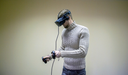 Man in helmet virtual reality plays game. Man uses VR-headset display with headphones for virtual reality game in office. High-tech devices. Augmented reality device creating virtual spaceの写真素材