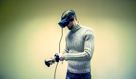 Man in helmet virtual reality plays game. Man uses VR-headset display with headphones for virtual reality game in office. High-tech devices. Augmented reality device creating virtual spaceの写真素材