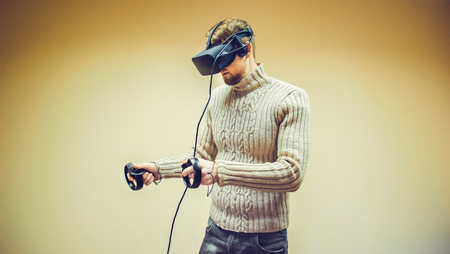 Man in helmet virtual reality plays game. Man uses VR-headset display with headphones for virtual reality game in office. High-tech devices. Augmented reality device creating virtual spaceの写真素材