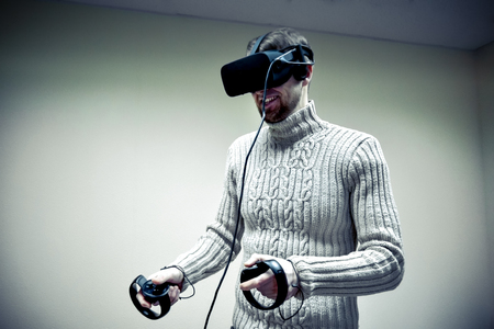 Man in helmet virtual reality plays game. Man uses VR-headset display with headphones for virtual reality game in office. High-tech devices. Augmented reality device creating virtual spaceの写真素材