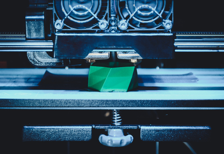 3D printer works and creates an object from the hot molten plastic close-up. Automatic three dimensional 3d printer performs plastic green colors modeling in laboratory.の写真素材