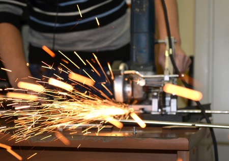 Worker man cutting a metal pipe in two pieces and lot of sparks flying straight into the camera close-up.の写真素材