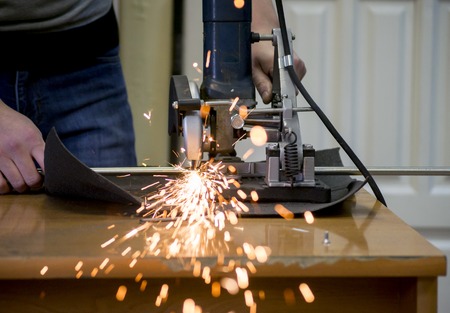 Worker man cutting a metal pipe in two pieces and lot of sparks flying straight into the camera close-up.の写真素材
