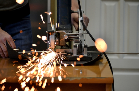 Worker man cutting a metal pipe in two pieces and lot of sparks flying straight into the camera close-up.の写真素材