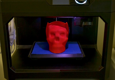 Skull printed with plastic of red color on a 3d printer. Inside 3d printer, black background