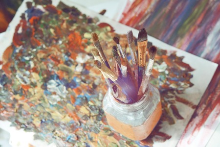 Brushes for drawing stand in a glass with a bristle upwards in a picture from smears with oil paints.の写真素材