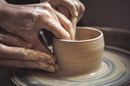 Creating vase of white clay close-up. Master crock.The sculptor in the workshop makes a jug out of earthenware closeup. Twisted potters wheel. Man hands making clay jug macro.の写真素材