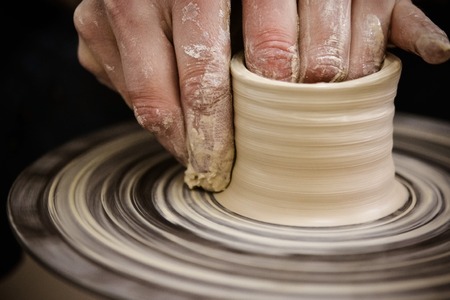 Creating vase of white clay close-up. Master crock.The sculptor in the workshop makes a jug out of earthenware closeup. Twisted potters wheel. Man hands making clay jug macro.の写真素材