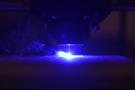 Laser engraving on wood macro. 3D printer laser beam burns the pattern close-up on a wooden board....