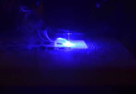 Laser engraving on wood macro. 3D printer laser beam burns the pattern close-up on a wooden board. Industrial Modern technological background. Laser blue 3d printer moves on a wooden surfaceの写真素材