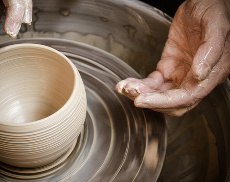 Hands of the master potter and vase of clay on the potter's wheel close-up. Master crock. Twisted potter's wheel.の写真素材