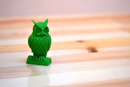 The model printed on a 3d printer. Object in the form of an owl of green color is on the table....