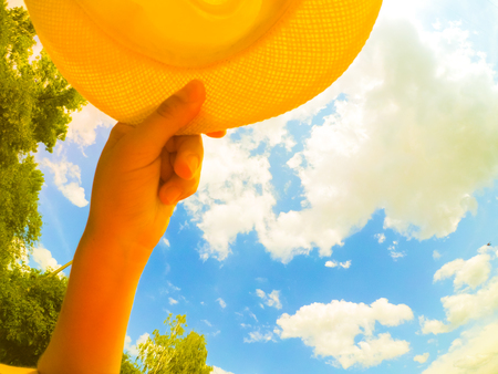 A man of Caucasian race holds a hat in his hand. On the background of sky and white clouds. Abstract concept of summer vacation holiday. Bottom view.の写真素材