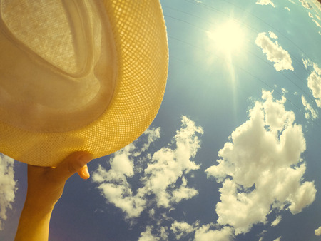 A man of Caucasian race holds a hat in his hand. On the background of sky and white clouds. Abstract concept of summer vacation holiday. Bottom view.の写真素材