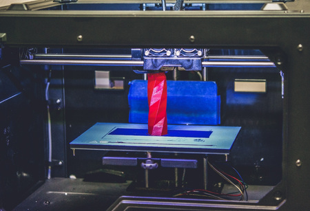 3D printer works and creates an object from the hot molten plastic close-up. Automatic three dimensional 3d printer performs plastic red colors modeling in laboratory.の写真素材