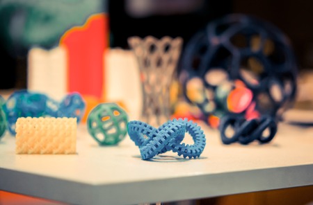Many abstract models bright colorful objects printed on a 3d printer on a white table.の写真素材