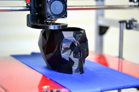 3D printer printing a model in the form of black skull close-up. The 4ht industrial revolution. Automatic three dimensional performs plastic modeling. Progressive modern additive technologyの写真素材