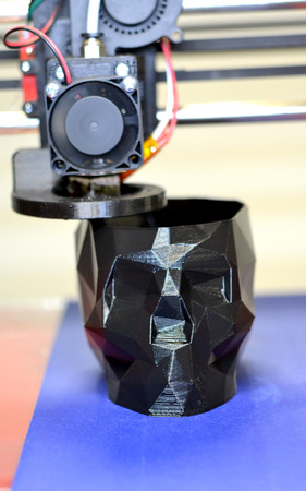 3D printer printing a model in the form of black skull close-up. The 4ht industrial revolution....