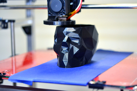 3D printer printing a model in the form of black skull close-up. The 4ht industrial revolution. Automatic three dimensional performs plastic modeling. Progressive modern additive technologyの写真素材