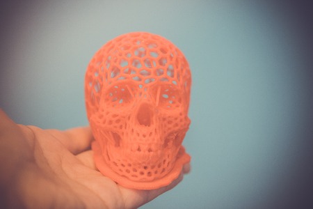 Skull printed with plastic of red color on a 3d printer. Skull printed on 3d printer in mans hand. Progressive modern additive technologyの写真素材