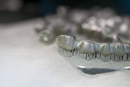 Object printed on metal 3d printer, laser sintering machine for metal close-up. Metal dental crowns sprinkled with metal powder after raising the platform in working chamber. DMLS, SLM, SLS technologyの写真素材