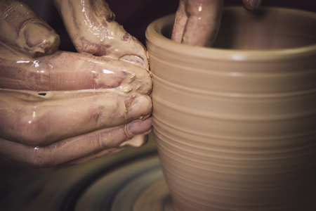 Creating ceramic products of white clay close-up. The sculptor in workshop makes clay jug closeup. Master crock. Twisted potters wheel. Art creativity Cultural tradition Handmade Craft Masters Handsの写真素材