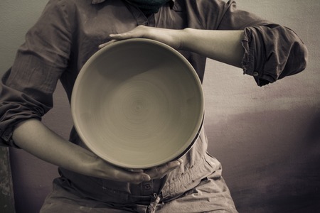 Master Potter holds round clay plate in his hands.Potters body. Sculptor sculpts pots products from white clay. Workshop pottery. Master crock. Creativity. Cultural traditions. Handmade. Craftの写真素材