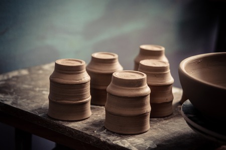 Ceramic clay products stand on the shelf close-up. Sculptor sculpts pots products from white clay. Workshop pottery. Dark image. Master crock. Creativity. Cultural traditions. Handmade. Craftの写真素材