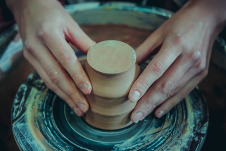 Creating ceramic products of white clay close-up. The sculptor in workshop makes clay jug closeup. Master crock. Twisted potters wheel. Art creativity Cultural tradition Handmade Craft Masters Handsの写真素材