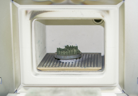 Object printed on metal 3d printer in the kiln for sintering after heat treatment synterization close-up. Dental crowns created in laser sintering machine. DMLS, SLM, SLS technology.の写真素材