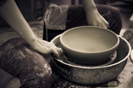 Master Potter holds round clay plate in his hands. Sculptor sculpts pots products from white clay. Workshop pottery. Master crock. Art, creativity. Cultural traditions. Handmade. Craft.の写真素材