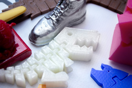 Many bright multi-colored objects printed on 3d printer lie on flat surface close-up. Fused...