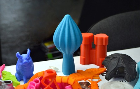 Many bright multi-colored objects printed on 3d printer lie on flat surface close-up. Fused...