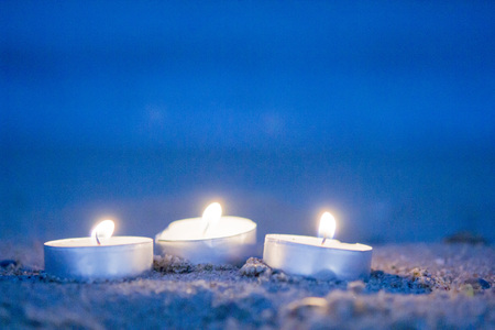 Three small candles tablets lie on a sandy beach near the waves with foam lapping on shore in the evening close-up. Romance mood background.の写真素材