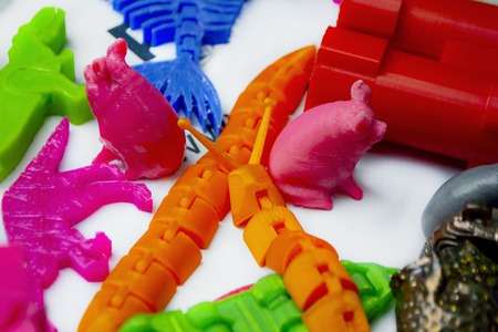 Many bright multi-colored objects printed on 3d printer lie on flat surface close-up. Fused...