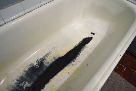 Very old rusty shabby bath close-up. A bath with peeling white enamel. Water flows in an old dirty bathtub. Black rusted dirty bath. Drain water in the rusty bathroom.の写真素材
