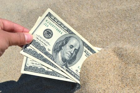 A girl takes out from the sand money notes of three hundred dollars. Concept finance money holiday relax vacation. Sunny summer warm day. A man takes out dollars from sand buried money banknotesの写真素材