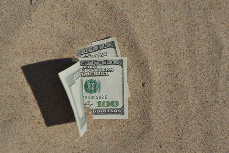 Money dollars half covered with sand lie on beach close-up. Dollar bills partially buried in sand. Three hundred dollars buried in sand on sea ocean beach Concept finance money holiday relax vacationの写真素材
