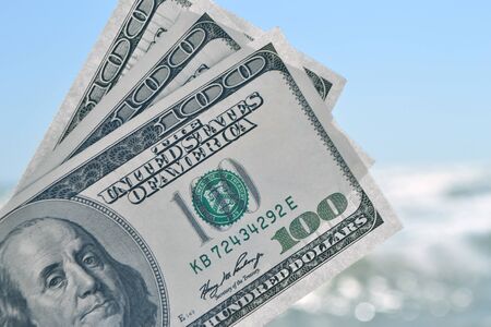 Girl holding money bill of 300 dollars on background of sea ocean waves and blue sky close-up. Hand...