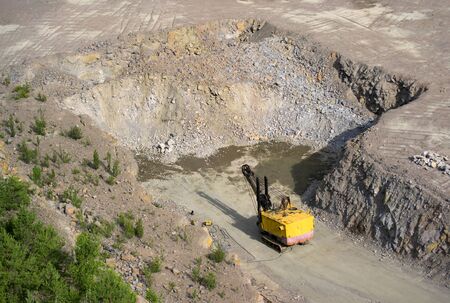yellow excavator carver is on the ground in front of granite stones in the quarry for granite