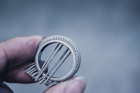 Man is holding object printed on metal 3d printer. Object printed in laser sintering machine. Modern 3D printer printing from metal powder. Progressive additive DMLS, SLM, SLS 3d printing technologyの写真素材
