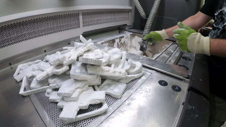 Man cleans details printed on industrial 3D printer from white plastic powder.の写真素材