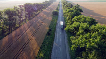 Aerial drone view flight over highway wheat field and green trees at sunset dawn