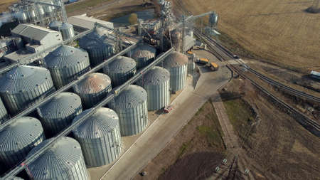 Truck full of grain rides near large metal silos of grain elevator on sunny day.の写真素材