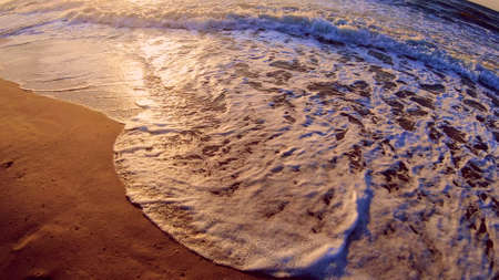 Sea wave with white foam rolls over sandy shore of beach. Top view.
